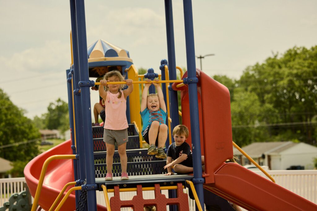 Three early childhood students play together on the playground equipment.