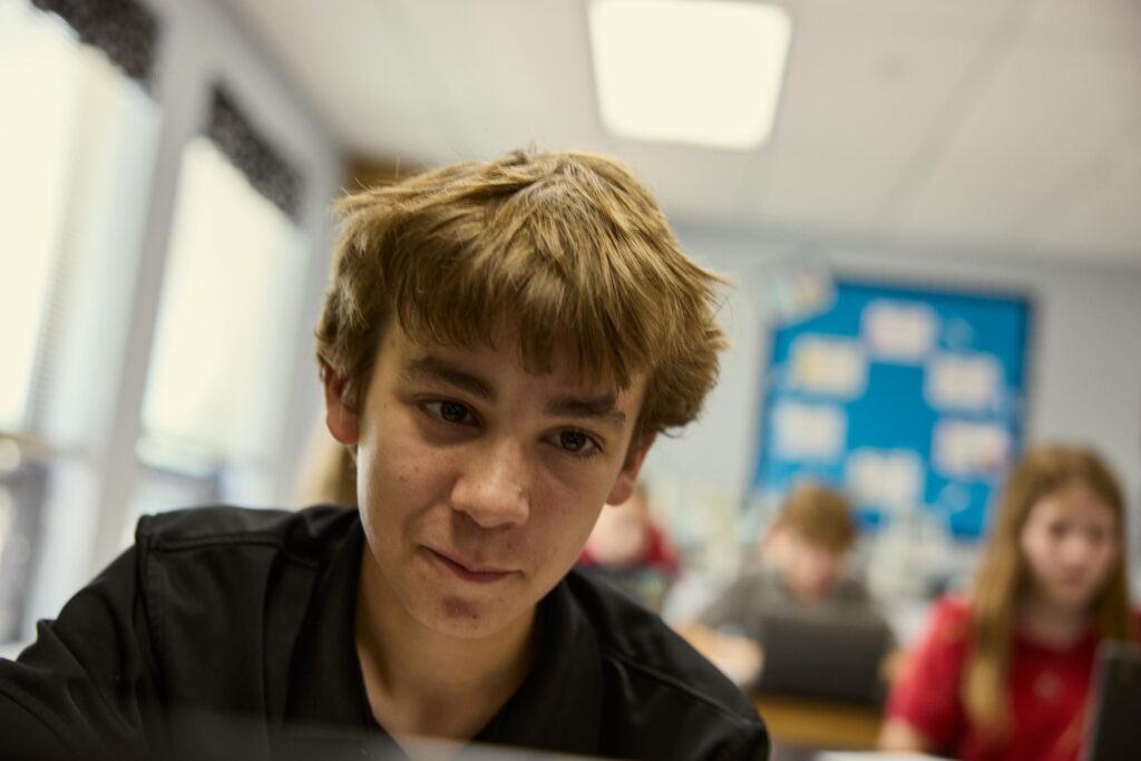 Middle school boy gives a small smile as he looks just past the camera in classroom.