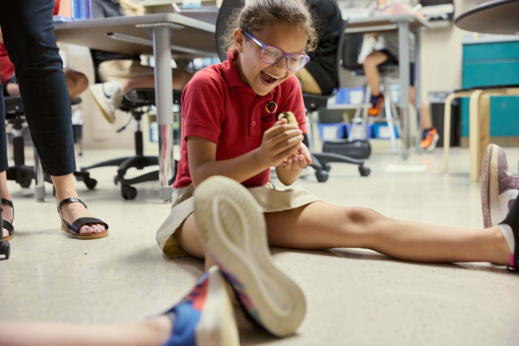 Elementary student exclaims in joy as she holds a baby chick in the classroom.