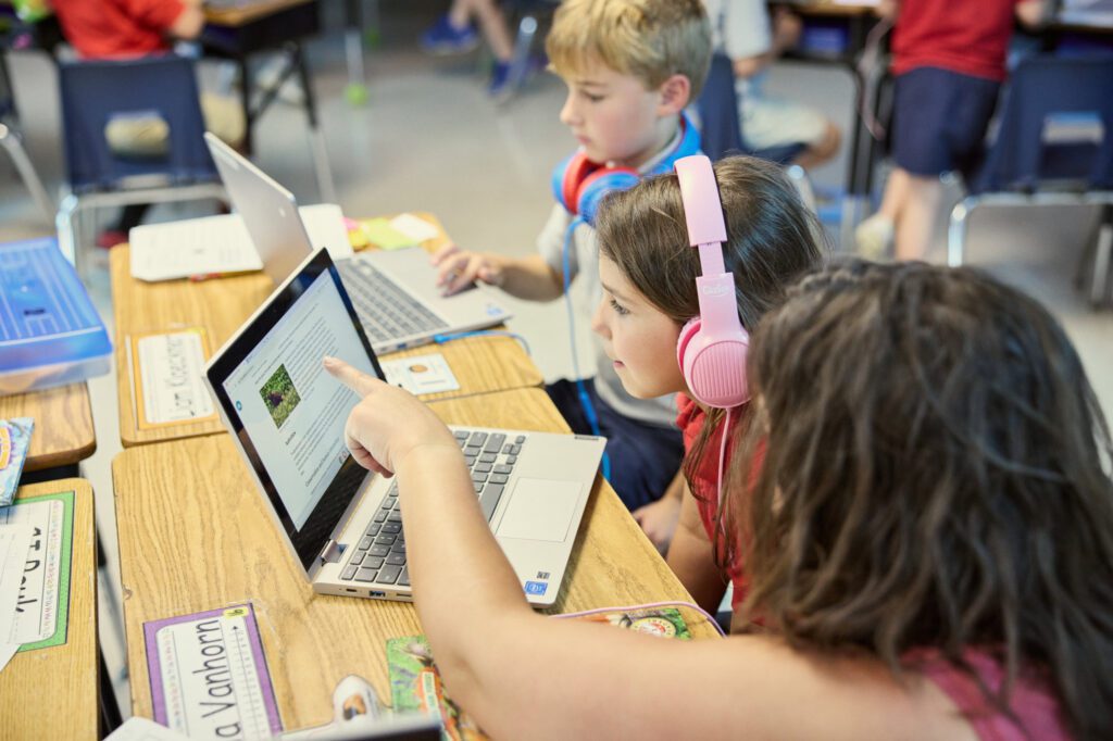 Three Elementary students sit at a desk working at a computer together.