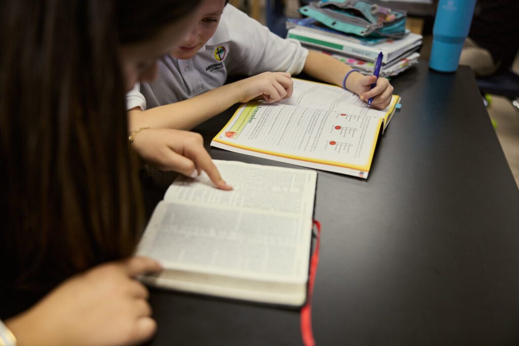 Students read Bible together at table.