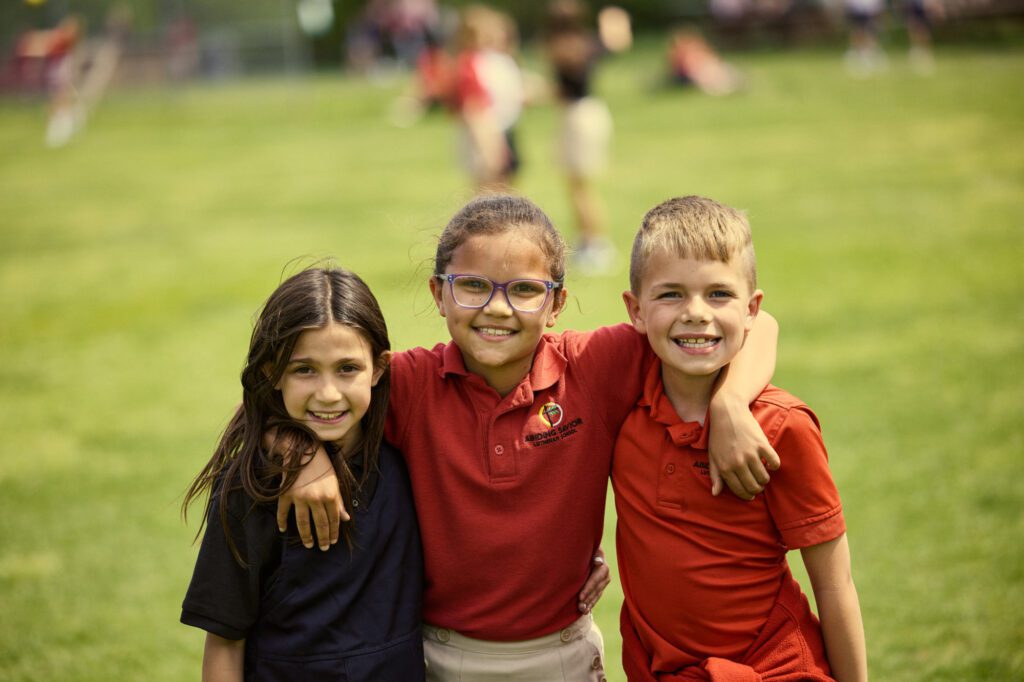 Three Elementary students with their arms around each other smile at the camera.