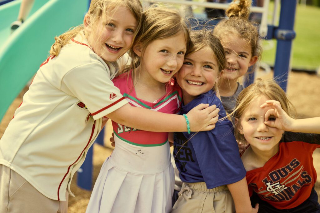 A group of Kindergarten-age girls embrace on the playground.