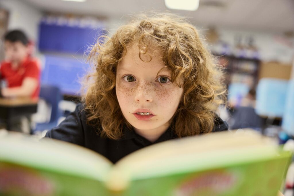 An elementary student focuses intensely whilst reading a book in class.