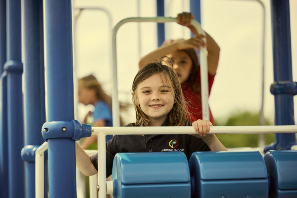 Young students at Abiding Savior Lutheran School smile for a photo as they play on the school playground.