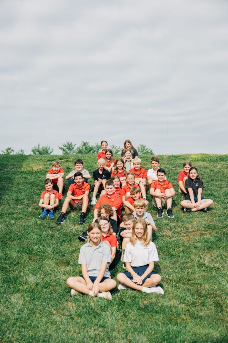 Students at Abiding Savior Lutheran School smile for an outdoor group photo on a grass covered hill.