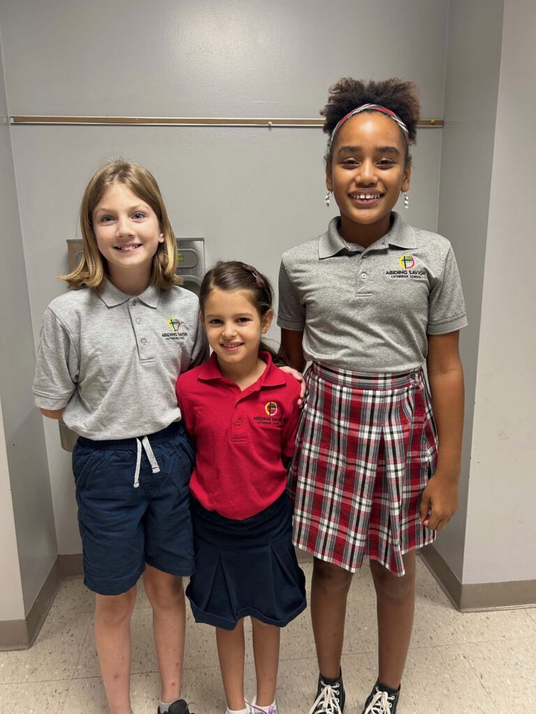 Three Elementary students smile with arms around one another before going into a chapel service at Abiding Savior Lutheran School.